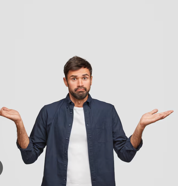 A man with a neatly trimmed beard and dark hair, wearing a dark blue button-up shirt over a white t-shirt, stands against a plain, light gray background. His eyebrows are raised, eyes wide, and mouth slightly downturned in a classic expression of bewilderment or confusion. Both of his hands are open and raised slightly, palms up, in a universal 'I don't know' or 'What can you do?' shrug. The stark, empty background humorously amplifies his perplexed demeanor, suggesting he's utterly baffled by something that isn't even in the frame. He embodies the universal feeling of being utterly clueless, making him a relatable figure for anyone who's ever asked, 'Seriously, what now?'