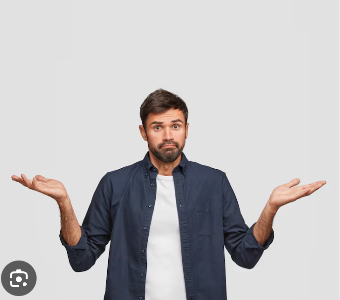 This image features a man with a bewildered and slightly confused expression, shrugging his shoulders with palms open, as if to say, "I don't know" or "What can you do?" He has dark hair and a neatly trimmed beard, wearing a dark blue button-up shirt over a white t-shirt. His wide eyes and slightly pursed lips perfectly convey a universal sense of mild exasperation or uncertainty. The plain, light grey background is entirely neutral, serving only to highlight the man's expressive gesture and demeanor, emphasizing his relatable confusion without any distracting elements. The humor lies in the sheer universality of his 'everyman' shrug, making him a perfect visual representation of life's many unanswered questions, or perhaps just forgetting where he left his keys.
