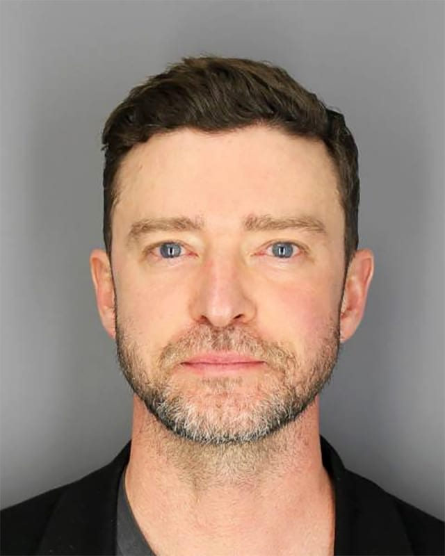 This image is a mugshot of famous musician and actor Justin Timberlake. He presents a neutral, slightly somber expression, looking directly into the camera with his blue eyes. His hair is dark and styled, and he has a short, well-maintained beard. The plain, light grey background is characteristic of a police booking photo, immediately setting the context of an arrest. This widely circulated image contrasts sharply with his usual polished public persona, offering a glimpse of a pop icon in an unglamorous, real-world situation. The humor arises from the unexpected sight of a celebrity known for upbeat anthems in such a stark, official setting.