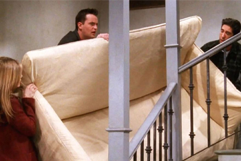 The image captures a comedic moment from the iconic TV show "Friends," where Ross, Monica, and Chandler are hilariously struggling to maneuver a large, beige couch up a staircase. Ross is at the front, looking intensely focused yet frustrated, while Chandler’s expression reflects a mix of determination and bewilderment. Monica, standing at the back, appears equally engaged, offering support while possibly providing instructions, underscoring the chaos of the scene.
The staircase is simple, with a railing that adds to the challenge of the couch's awkward positioning. This moment is emblematic of the show's humor, highlighting the friends' camaraderie amid absurd situations. The couch itself seems almost alive, resisting their efforts, which adds a layer of irony and humor to the struggle. Overall, this scene is a beloved example of the show's blend of friendship and comedic mishaps, making it a memorable pop culture moment.