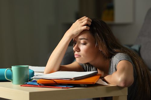 In this image, a young woman appears deeply frustrated, resting her forehead on her hand while surrounded by scattered study materials on a table. Her expression conveys exhaustion and stress, likely stemming from an overwhelming workload or intense study session. The casual setting suggests a home environment, with a hint of warmth from the soft lighting.
The background is somewhat blurred, indicating a cozy yet cluttered space, possibly with bookshelves or personal items that add to the sense of a student's life.
This scene humorously captures the relatable struggle of academic pressures—akin to a meme of the "struggling student" trope. The teal mug hints at the caffeine-fueled late-night study sessions, while the colorful folders seem to mock her efforts, almost as if they’re saying, "Good luck with that!" It's a snapshot of life that resonates with students everywhere.