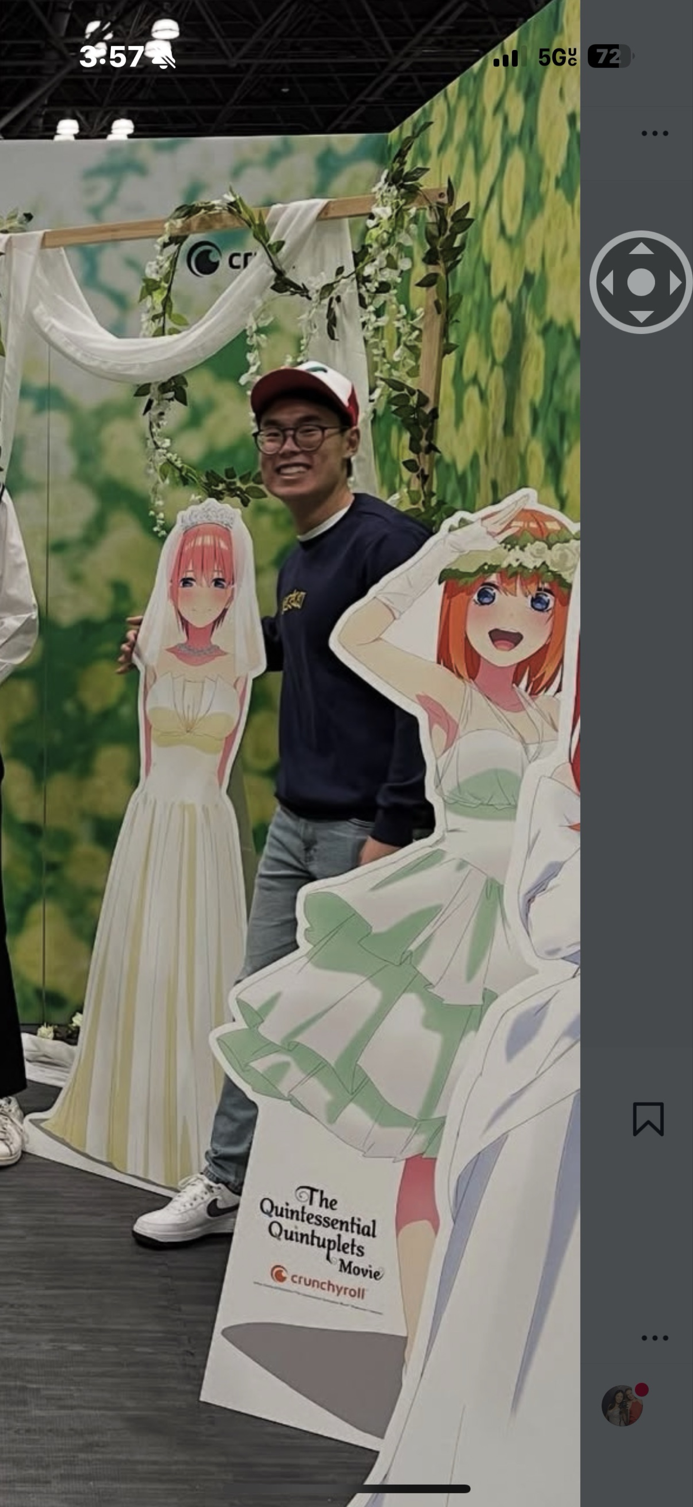 In the image, a cheerful individual stands next to life-sized cutouts of characters from "The Quintessential Quintuplets," a popular anime film. The subject, wearing glasses and a red and white cap, beams with excitement, embodying the playful spirit of anime fandom. He poses with two of the sisters, one in a white dress and the other in a green dress, both adorned with floral headpieces.

The background features a vibrant green floral setup, enhancing the whimsical atmosphere of a promotional event. The presence of the Crunchyroll logo hints at the anime’s streaming service, connecting the scene to a larger context of anime culture. 

Humorously, it appears as if the cutouts are his animated companions, making for a fun and lighthearted photo op, as if they’re all part of a quirky family reunion!