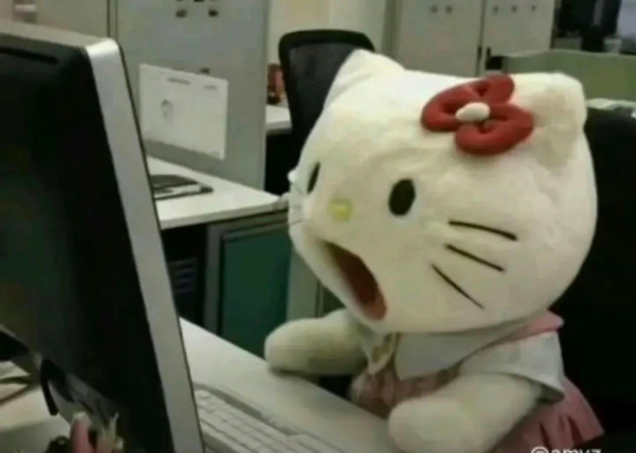 This iconic image captures a person in a Hello Kitty mascot costume, known for her red bow, sitting at a computer in what appears to be an office cubicle. The subject's demeanor is one of extreme shock or surprise, with their mouth agape, creating a highly humorous and relatable expression. The background, featuring a typical office setup with a monitor, keyboard, and cubicle walls, perfectly contrasts with the whimsical character, amplifying the comedic effect. This scene is widely recognized as the "Hello Kitty Shocked Meme," where the beloved Sanrio character is anthropomorphized into a state of disbelief, likely reacting to something unexpected on the screen. The humor stems from seeing a cheerful cartoon character in such a human, startled predicament within a mundane work environment.