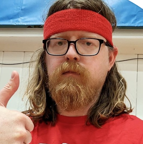 The image showcases a man with long hair and a full beard, wearing a red headband and glasses, giving a thumbs-up gesture. His expression is serious yet slightly comical, as he appears to be earnestly endorsing something, possibly a sporting event or fitness activity. The red headband adds a playful touch, evoking nostalgia for 80s workout culture.
In the background, there is a hint of a gym or sports environment, suggested by the blue backdrop and the wall structure, which enhances the overall context of physical activity. This setting invites thoughts of spirited competitions or casual games, fitting for someone ready to cheer on a team.
The combination of his serious demeanor and the playful attire creates a humorous juxtaposition, making the image both relatable and amusing, reminiscent of motivational posters gone awry. It's as if he's about to lead an intense workout while maintaining a deadpan charm.