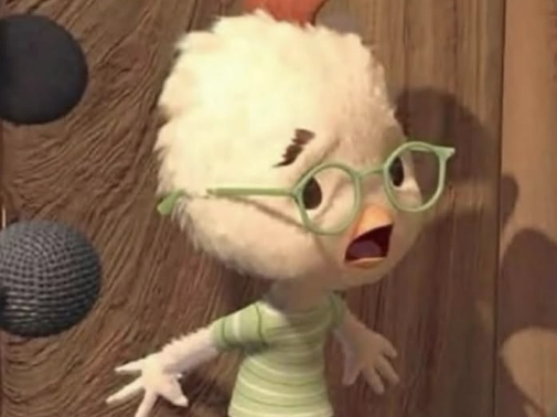 The image shows an animated character that appears to be a small white bird with fluffy feathers. The bird is wearing green glasses and a light green striped shirt. It has an expressive face with its mouth open, possibly indicating surprise or speaking. The background consists of a wooden surface with some round, textured objects attached to it.