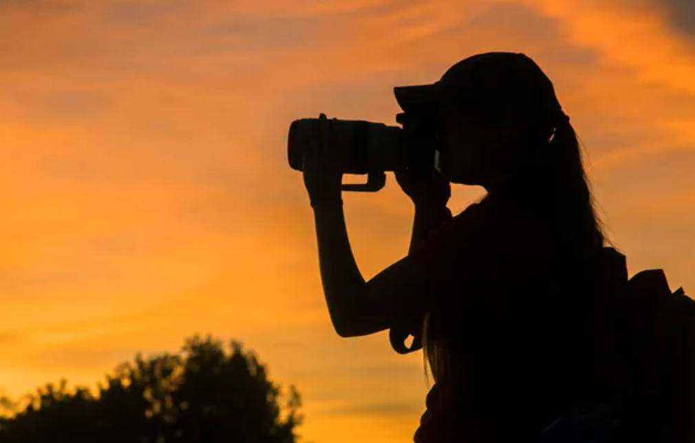 In this image, a person is silhouetted against a stunning sunset, their camera raised as if capturing the vibrant colors of the sky. The subject's demeanor appears focused and contemplative, embodying a moment of artistic inspiration. The warm tones of orange and yellow in the background create a dramatic contrast with the dark outline of the figure, enhancing the scene's beauty. The silhouette suggests an adventurous spirit, perhaps a photographer on a quest to capture nature's fleeting moments.
The background, with its soft clouds and fading light, sets a serene tone, evoking a sense of tranquility and wonder. This could symbolize the pursuit of creativity and the importance of appreciating the world around us. It's a reminder that sometimes the most breathtaking scenes are best captured through the lens of curiosity.