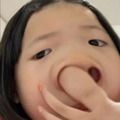The image presents a close-up of a young child, likely female, with dark hair, captured in a moment of pure, unadulterated silliness. A hand, possibly their own, playfully pushes up their nose, comically distorting their face. Their eyes are wide and slightly upturned, adding to the mischievous and exaggerated expression, clearly indicating a playful demeanor. The humor stems from the delightful facial contortion and the child's evident enjoyment of the funny face. The background is a simple, out-of-focus light-colored wall, providing a neutral backdrop that keeps the focus entirely on the child's amusing antics. This common humorous visual, while not from a specific show, movie, or cultural event, perfectly encapsulates a universal moment of childhood fun.