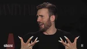 The image features a man with a well-groomed beard, expressive demeanor, and long, stylized nails, which adds a humorous contrast to his otherwise masculine appearance. He seems animated, gesturing with his hands while perhaps sharing a funny story or making a point, suggesting a lively conversation. The background is blurred, likely indicating a casual interview or promotional setting, possibly related to a movie or television show, given the context of his attire and expression.
The visual humor lies in his exaggerated gestures and the unexpected combination of his masculinity with flamboyant nails, creating a playful juxtaposition. This image could evoke laughter as it challenges traditional gender norms in a lighthearted way, making it relatable and shareable. The overall vibe is one of fun, and it appears to be a candid moment that captures his personality and charm.