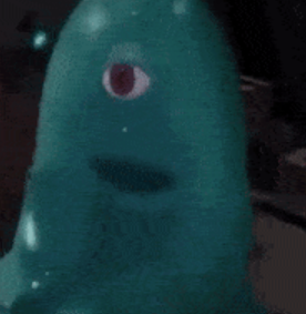 This image features a close-up of B.O.B. (Bicarbonate Ostylezene Benzoate), the lovable, indestructible, and brainless blob from the DreamWorks animated movie 'Monsters vs. Aliens.' The subject is a vibrant teal, gelatinous creature with a single, prominent red eye that seems to gaze with a mix of innocent curiosity and mild bewilderment. Below its eye, a dark, oval-shaped opening serves as its mouth, adding to its simple, almost childlike expression. Its demeanor is inherently humorous, embodying a cheerful lack of understanding. The background is dark and indistinct, suggesting an indoor setting, likely a controlled environment or a scene from the movie where the focus is entirely on B.O.B. The humor stems from his perpetually surprised look and his iconic, squishy form, making him an instantly recognizable and endearing character.
