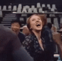 The GIF features actress Scarlett Johansson caught in a moment of pure, uninhibited laughter, her head thrown back and mouth wide open in an expression of overwhelming amusement. Her eyes are crinkled with joy, and she appears to be wearing a dark, patterned top. This candid and infectious reaction shot has become a widely recognized popular meme, often used to convey extreme mirth or disbelief. The blurry background suggests a bustling public event, likely an audience or a large gathering in an indoor venue such as a talk show set or a press conference, where her spontaneous outburst stands out. The humor lies in the sheer intensity and relatable nature of her uncontrollable laughter.