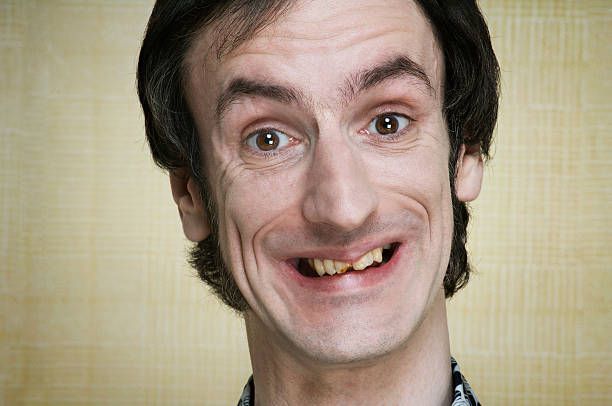 The image depicts a man with a quirky, wide smile, showcasing an unusual gap in his teeth. His demeanor is cheerful and slightly eccentric, suggesting a playful or humorous personality. The background appears to be a soft, textured beige, which emphasizes his expression and adds a lighthearted tone to the image.
His hairstyle and outfit give off a casual vibe, hinting at a comedic character, possibly from a sitcom or a sketch show. This combination of features, especially the toothy grin, evokes a sense of endearment and amusement, as if he’s just shared a funny joke.
The overall scene feels relatable and approachable, perhaps reminiscent of characters in comedic performances where humor thrives on the unexpected. There’s a charming awkwardness that invites laughter, making the subject memorable in a lighthearted way.