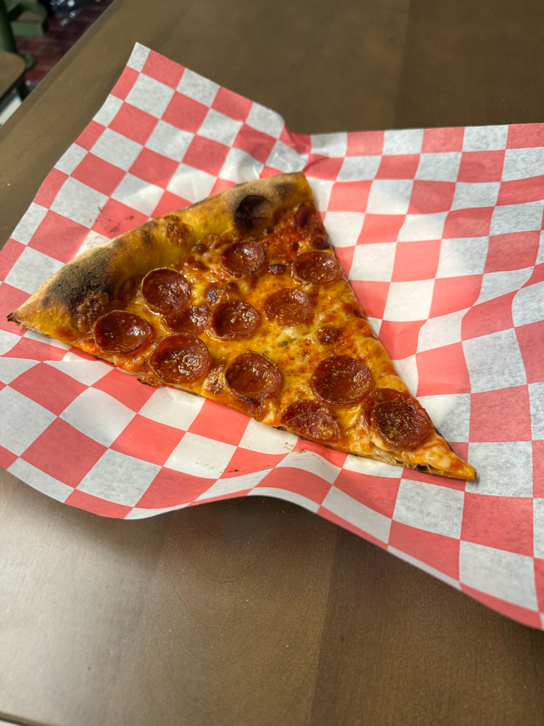 The image showcases a delicious slice of pepperoni pizza, resting on a vibrant red and white checkered paper, evoking a classic diner vibe. The pizza is perfectly cooked, with golden-brown crust edges and glistening, slightly crispy pepperoni pieces dotting the surface. 

The demeanor of this slice is inviting and playful, almost as if it’s beckoning you to take a bite. The background is a simple wooden table, enhancing the rustic feel, while the checkered paper adds a nostalgic touch, reminiscent of casual eateries or food trucks.

This scene doesn’t just tantalize the taste buds; it invites a sense of comfort and satisfaction. One can almost imagine the slice whispering, “Life is too short—grab a napkin and enjoy!” The humor in the scenario lies in the slice's exaggerated sense of importance, as if it's the main star of a culinary blockbuster!