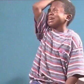 This iconic image captures the "Crying Kid Meme," featuring a young boy in a moment of profound, exaggerated despair. His face is contorted, eyes squeezed shut, mouth wide open in a wail, and tears stream down his cheeks. One hand is dramatically placed on his forehead, emphasizing his intense emotional distress. He wears a striped t-shirt with red, white, and blue hues. The plain, light blue background is simple and uncluttered, serving to highlight the boy's over-the-top reaction without distraction. This stark simplicity perfectly frames his theatrical sadness, making it a universally relatable and humorous depiction of minor inconveniences or "first world problems" blown out of proportion.