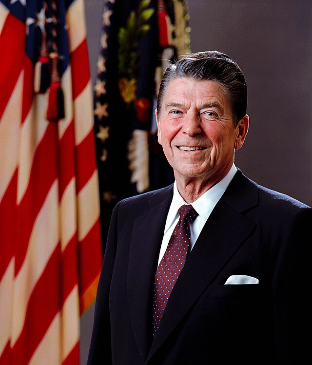 This official portrait features Ronald Reagan, the 40th President of the United States, exuding a warm and confident demeanor. He smiles broadly, his eyes twinkling, as if sharing a pleasant thought or a classic anecdote. Dressed impeccably in a dark suit, white shirt, and a patterned red tie with a crisp white pocket square, he embodies presidential gravitas. The background prominently features the American Flag on the left and the Presidential Seal Flag on the right, framing him perfectly and underscoring his high office. The flags are not just decor; they are integral symbols of his role, reinforcing the formal and patriotic context of the image. It's almost as if the flags are silently cheering him on, a fitting backdrop for a leader known for his optimism.