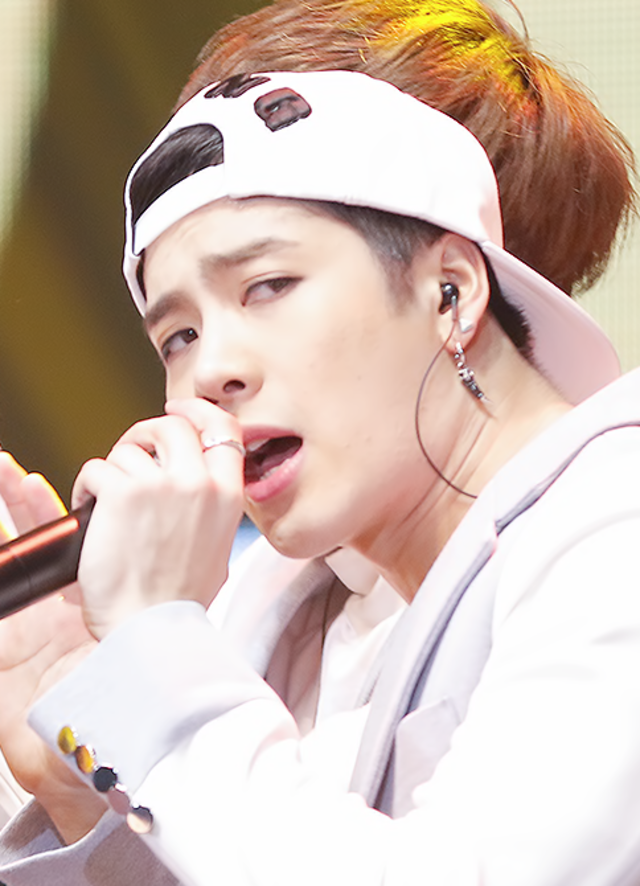 The image features a young male performer passionately singing into a microphone. He wears a white cap backwards, which adds a playful, youthful vibe, paired with stylish attire that includes a light-colored jacket. His expression conveys intensity and focus, suggesting he is fully immersed in his performance, capturing the attention of an audience.
The background is slightly blurred, hinting at a vibrant stage atmosphere, likely illuminated by colorful lights, enhancing the dynamic feel of the scene. This context suggests a live performance, perhaps at a concert or music festival, where energy and excitement are palpable.
Overall, the combination of his expressive demeanor and the lively backdrop creates a captivating moment, as if he’s inviting the audience to join in his musical journey. The playful cap, coupled with the intense expression, adds a humorous contrast—like a serious singer ready for a fun day at the park!