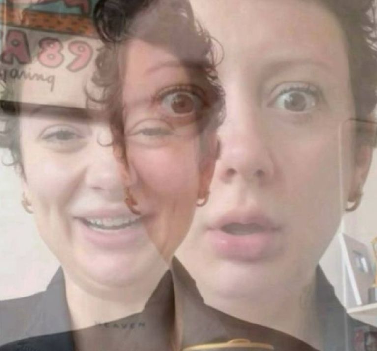 The image appears to feature a person with a layered, double-exposure effect, creating a surreal and intriguing visual. One side of the face shows a smiling expression, while the other displays a look of surprise or shock. This juxtaposition creates a humorous contrast, as if the person is experiencing two different emotions simultaneously.

The background is somewhat blurred, likely a plain or softly colored wall, which helps to emphasize the subject's expressions without distractions. There are hints of decor, such as a colorful poster or artwork, which adds a playful element to the scene.

Overall, the image captures a whimsical moment, suggesting an unexpected shift in mood. The playful nature of the expressions invites viewers to ponder the thoughts racing through the subject's mind, making it a delightful and engaging visual.