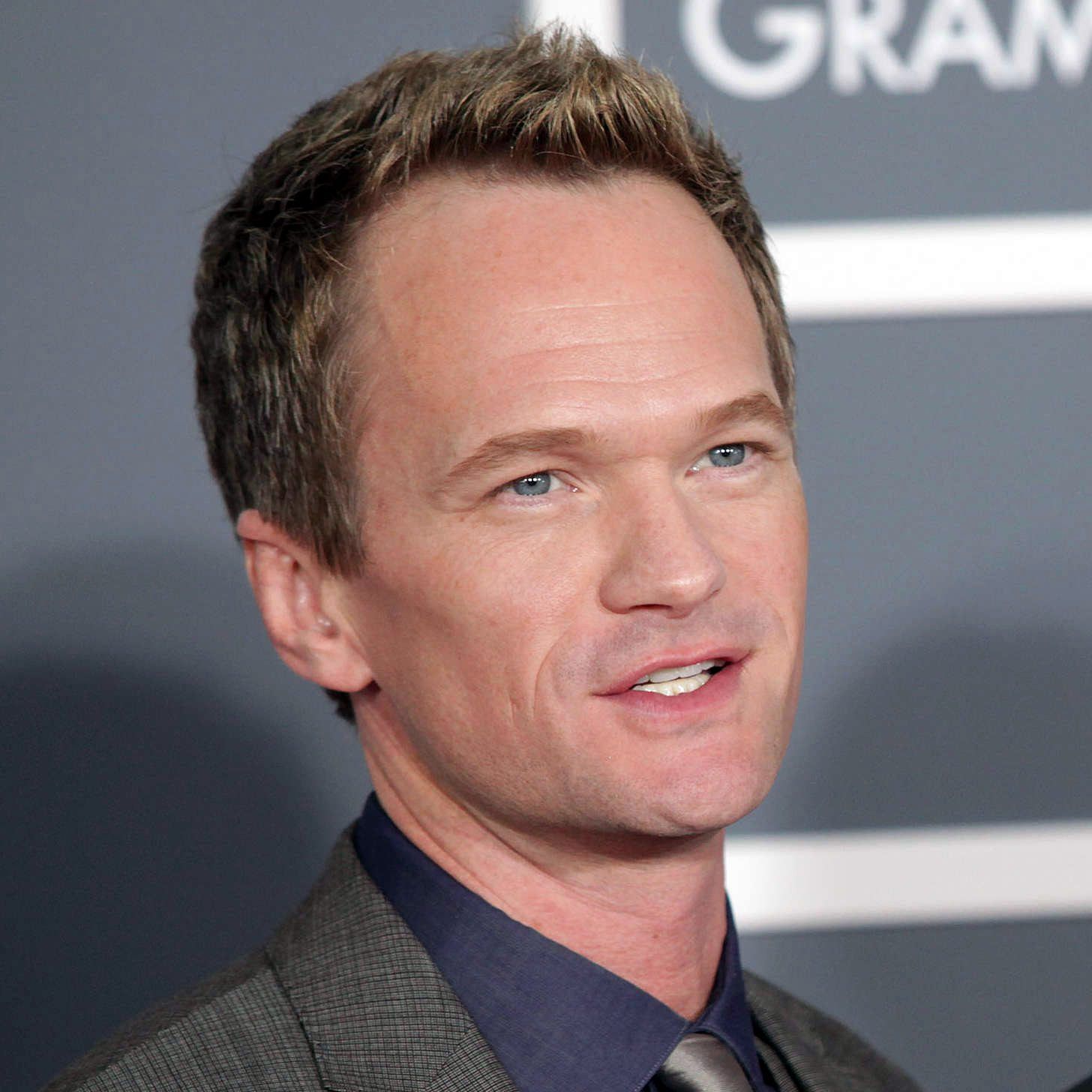 I’m so fed up with this overpolished, soulless photo-op. The lifeless gray backdrop with those chopped-off block letters is screaming brand before it says anything human. The lighting is sterile and flattening, buffing away texture until everything looks plastic. And that cookie-cutter suit-and-tie palette—steel on slate on more slate—couldn’t be more bland if it tried. It’s all pose, zero pulse: a carefully calibrated half-smile and a frame crammed just tight enough to sneak in some logo, like the entire image exists to be marketable instead of memorable. Glossy, sanitized, and boring—and that emptiness is infuriating.