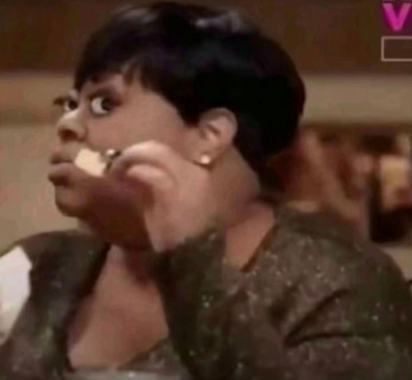 This iconic image captures Tiffany Pollard, also known as New York from the reality TV show "Flavor of Love," mid-chew with a piece of food near her mouth. Her demeanor is one of intense, wide-eyed suspicion and disbelief, perfectly embodying the famous "Tiffany Pollard Side-eye Meme." The humor stems from her exaggerated expression, which has become a universal reaction to incredulous situations. The blurry background, featuring a prominent "V" logo, strongly suggests the image is from VH1, the network that aired "Flavor of Love," directly linking it to her reality TV origins. Her expression is a masterclass in non-verbal communication, conveying a mix of judgment and confusion.