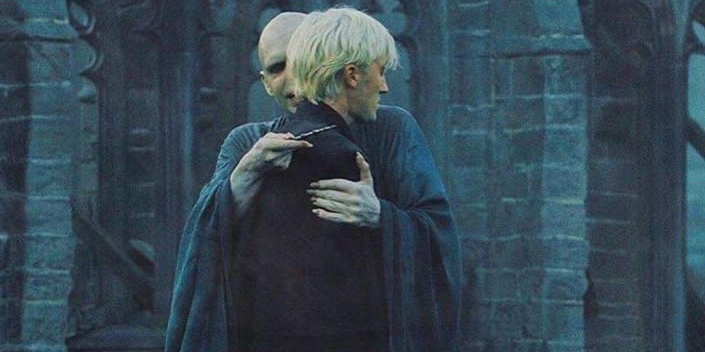 The image captures a tense moment from "Harry Potter and the Deathly Hallows," featuring Lord Voldemort and Draco Malfoy. Voldemort, with his pale skin and snake-like features, looms ominously over Draco, who appears conflicted and vulnerable. The contrasting postures suggest a complex dynamic, with Voldemort's grip firm yet unsettling, while Draco's demeanor reflects uncertainty and fear.
The background consists of dark, stone ruins, likely part of Hogwarts or a similar significant location, enhancing the scene's dramatic tension. This environment amplifies the gravity of their interaction, symbolizing the oppressive influence Voldemort wields over Draco.
The humor here lies in the absurdity of the situation: a dark lord seemingly offering an awkward embrace. It’s as if Voldemort is trying to channel his inner motivational speaker, while Draco just wants to escape to the nearest Gryffindor common room.