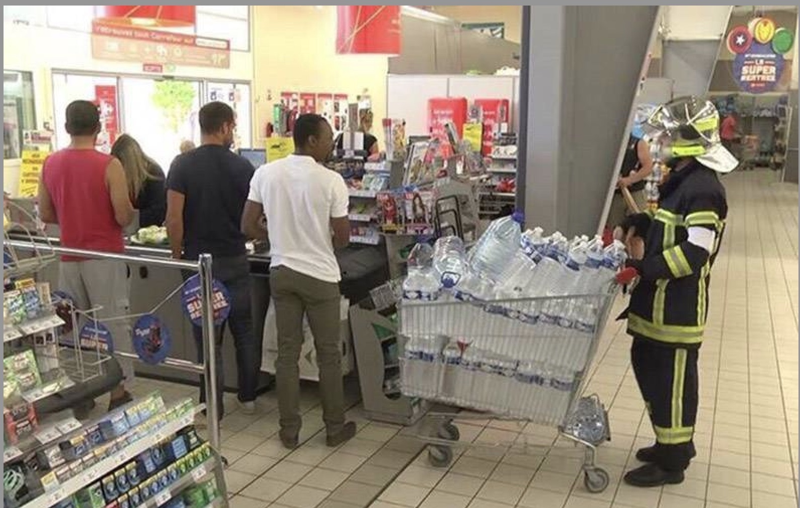 In a Carrefour supermarket, a firefighter in full uniform, complete with helmet, stands patiently in a checkout line, pushing a shopping cart overflowing with numerous large bottles of water. The scene presents a humorous juxtaposition: a hero typically associated with dousing flames is instead acquiring an impressive quantity of water from a grocery store. Other shoppers, seemingly unfazed, wait ahead, adding to the surreal normalcy of the situation. The firefighter's posture appears calm and determined, suggesting a serious, albeit unusual, mission. The background clearly shows a typical supermarket environment with checkout counters and shelves, emphasizing the unexpected presence of the emergency responder in such a mundane setting. It's a comical sight, perhaps indicating a very thirsty fire crew or a unique emergency requiring hydration rather than suppression.