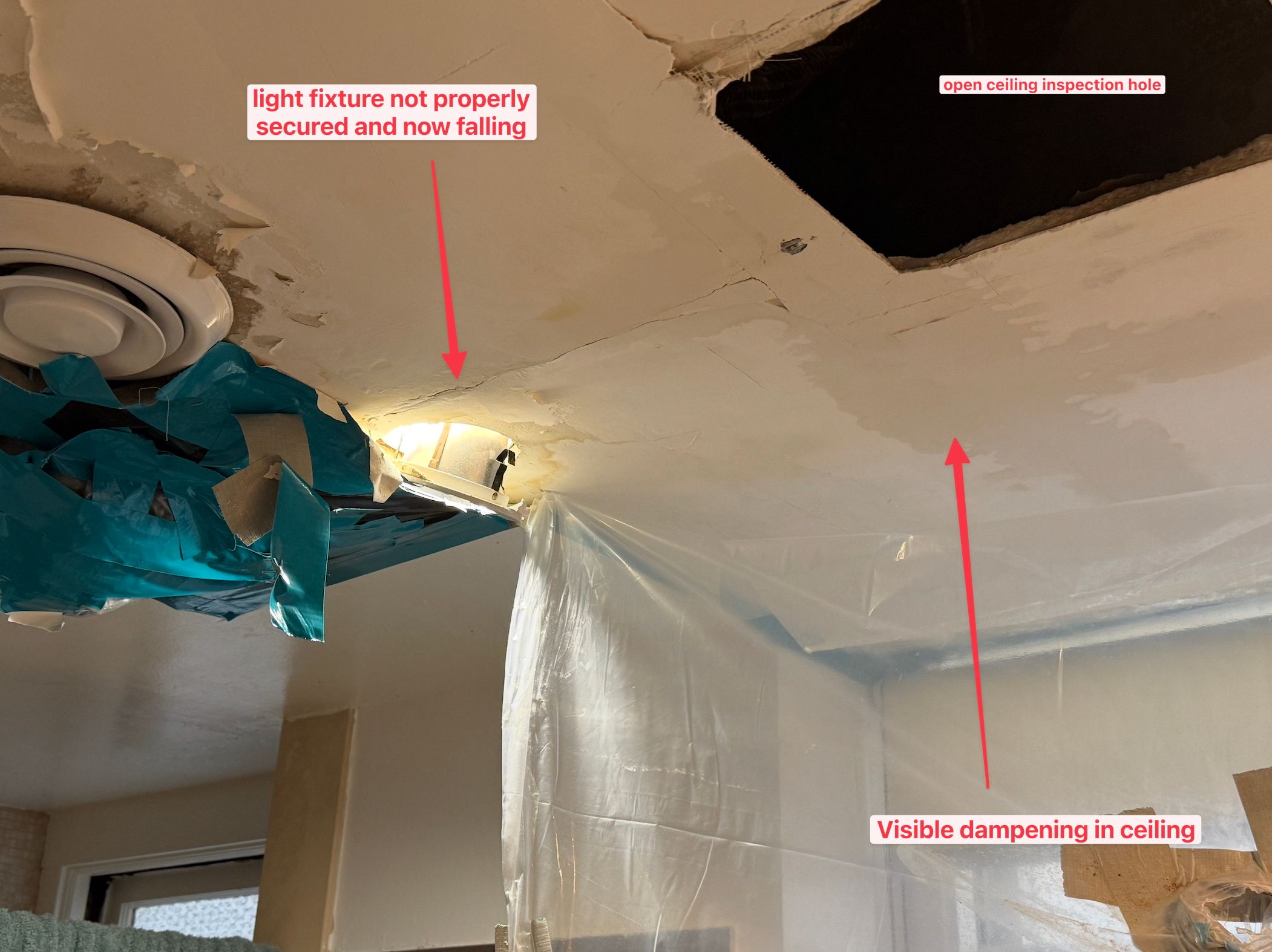 This image captures a ceiling in a state of dramatic disarray, looking utterly exasperated. The ceiling, like a weary old friend, is shedding its skin with peeling paint and plaster, revealing its age and distress. A light fixture, clinging precariously, seems to be making a desperate bid for freedom, barely holding on. Above, a gaping, dark inspection hole yawns like a surprised mouth, perhaps exclaiming, "Oh dear, what a mess!" Visible dampening stains add to its woes, suggesting a recent tearful outburst. Blue and clear plastic sheeting draped below hint at ongoing repairs or an attempt to contain the ceiling's emotional breakdown. This scene of domestic chaos, while clearly a repair in progress, offers a humorous glimpse into a ceiling's very bad day. I do not recognize any famous or recognizable content in this image.